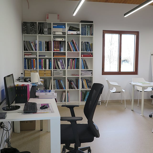 Una habitación con un escritorio de computadora y estantes con libros.