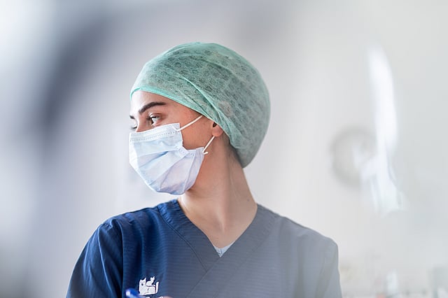 Una persona con una mascarilla quirúrgica y uniformes médicos.